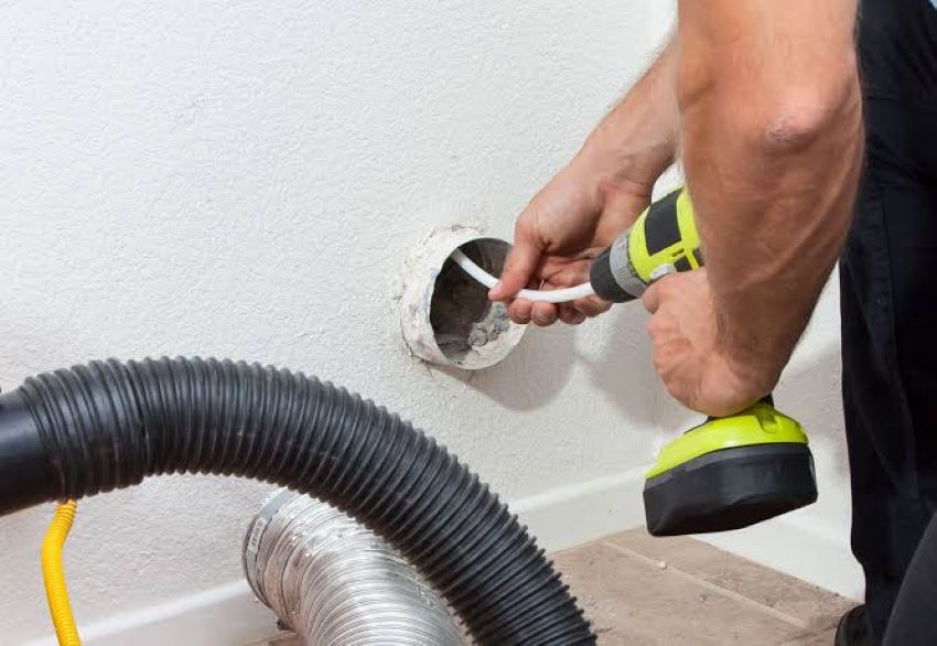 Person cleaning a dryer vent with a vacuum attachment to remove lint buildup